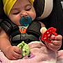 Arielle is registered to the contest to win money with this photo: baby, pacifier, yellow_bow, car_seat, blanket, toy, infant, child, sleepy, cute, hand, clothing, seatbelt, comfort, pink, red, green, indoor, face, headwear