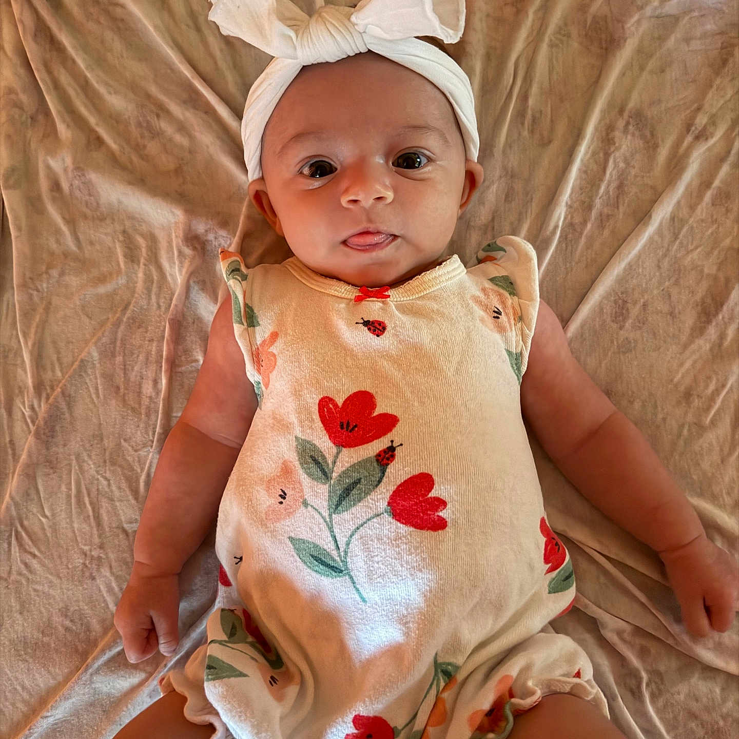 Blakely joined the competition — help win amazing prizes! baby, infant, child, romper, headband, bow, flower_pattern, skin, lying_down, bed_sheet, fabric, cute, playful, tongue_out, small_hands, small_legs, soft_lighting, portrait, indoors, person