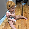 toddler, child, beanie, hat, floor, wooden_floor, indoor, sitting, clothing, toy, playful, person, room, bed, game_box, expression, casual, cute, young_child, home