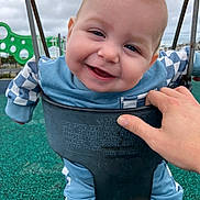 Gavin is registered to the contest to win money with this photo: baby, infant, child, swing, playground, smile, happy, face, hand, caregiver_hand, clothing, blue_outfit, outdoors, sky, rubber_surface, play_equipment, seat, eyes, cheeks, portrait