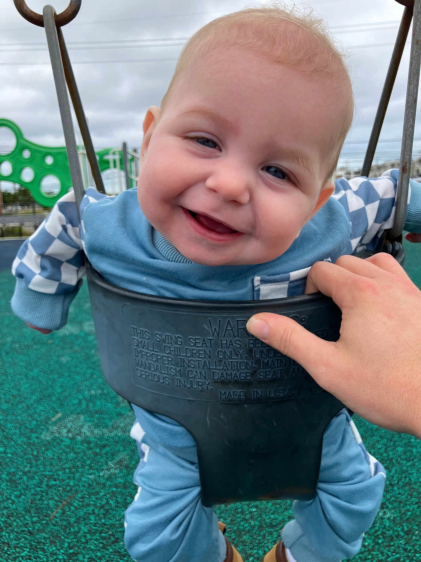 Gavin is registered to the contest to win money with this photo: baby, infant, child, swing, playground, smile, happy, face, hand, caregiver_hand, clothing, blue_outfit, outdoors, sky, rubber_surface, play_equipment, seat, eyes, cheeks, portrait