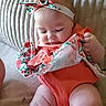 baby, infant, child, orange_outfit, headband, floral_pattern, cloth, cushion, texture, skin, cute, indoors, sitting, curious, soft_light, portrait, person, hand, legs, closeup