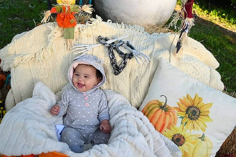 Octavia is registered to the contest to win money with this photo: baby, baby_toddler_clothing, calabaza, child, comfort, cucurbita, event, fun, grass, happy, headwear, leisure, linens, orange, person, plant, pumpkin, recreation, sitting, textile