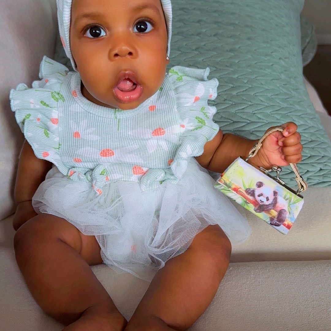 Leilany joined the competition — help win amazing prizes! baby, child, infant, cute, surprised, headband, ruffled_dress, purse, panda, couch, cushion, indoor, person, sitting, soft_lighting, expression, small_handbag, adorable, portrait, home