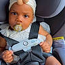 baby, child, car_seat, pacifier, headband, flower, white_clothing, safety_harness, seatbelt, infant, cute, portrait, indoors, child_safety, serious_expression, toddler, cute_accessory, straps, car_interior, small_hands