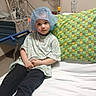 Thomas joined the competition — help win amazing prizes! child, hospital, bed, pillow, medical_equipment, gown, surgical_cap, curious, sitting, indoor, healthcare, young, person, medical_room, patient, hospital_gown, colorful_pillow, white_sheet, cords, medical_device