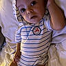 baby, infant, striped_onesie, hood, bed, white_sheets, looking_up, hand_on_head, curious, cute, child, young, portrait, indoors, person, sleepwear, relaxed, small, adorable, toddler
