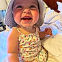 baby, child, smiling, hat, romper, bed, indoor, cute, happy, infant, person, clothing, skin, face, baby_teeth, sitting, white_bedding, lamp, room, portrait