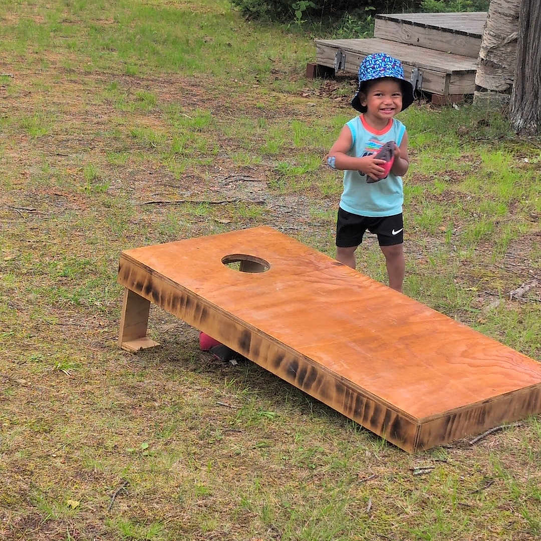 Zehri is registered to the contest to win money with this photo: casual_clothing, child, cornhole, deck, football, fun, game, grass, happy, hat, nature, outdoor, play, recreation, smile, sport, summer, trees, wooden_board, young