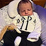 baby, infant, sleeping, clothing, white_shirt, black_pants, soft_toy, baby_seat, cushion, wooden_background, indoors, child, cute, peaceful, newborn, portrait, face, hand, foot, resting