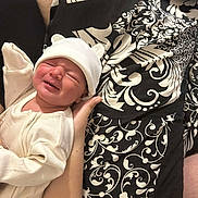Amelia is registered to the contest to win money with this photo: baby, newborn, infant, white_clothing, hat, cute, crying, hand, patterned_fabric, black_and_white, person, skin, lying_down, soft_light, closeup, cozy, sleepy, small, human, indoors