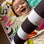 baby, smiling, play_mat, toy_bar, striped, infant, happy, child, colorful, music_notes, animal_print, striped_toy, indoor, floor, cute, clothing, striped_clothes, person, portrait, closeup