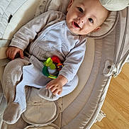 Adam participe au concours pour gagner de l'argent avec cette photo : baby, infant, pajamas, toy, baby_rocker, smiling, face, cushion, floor, wooden_floor, hand, footwear, head, person, indoor, comfort, child, play, clothing, happy