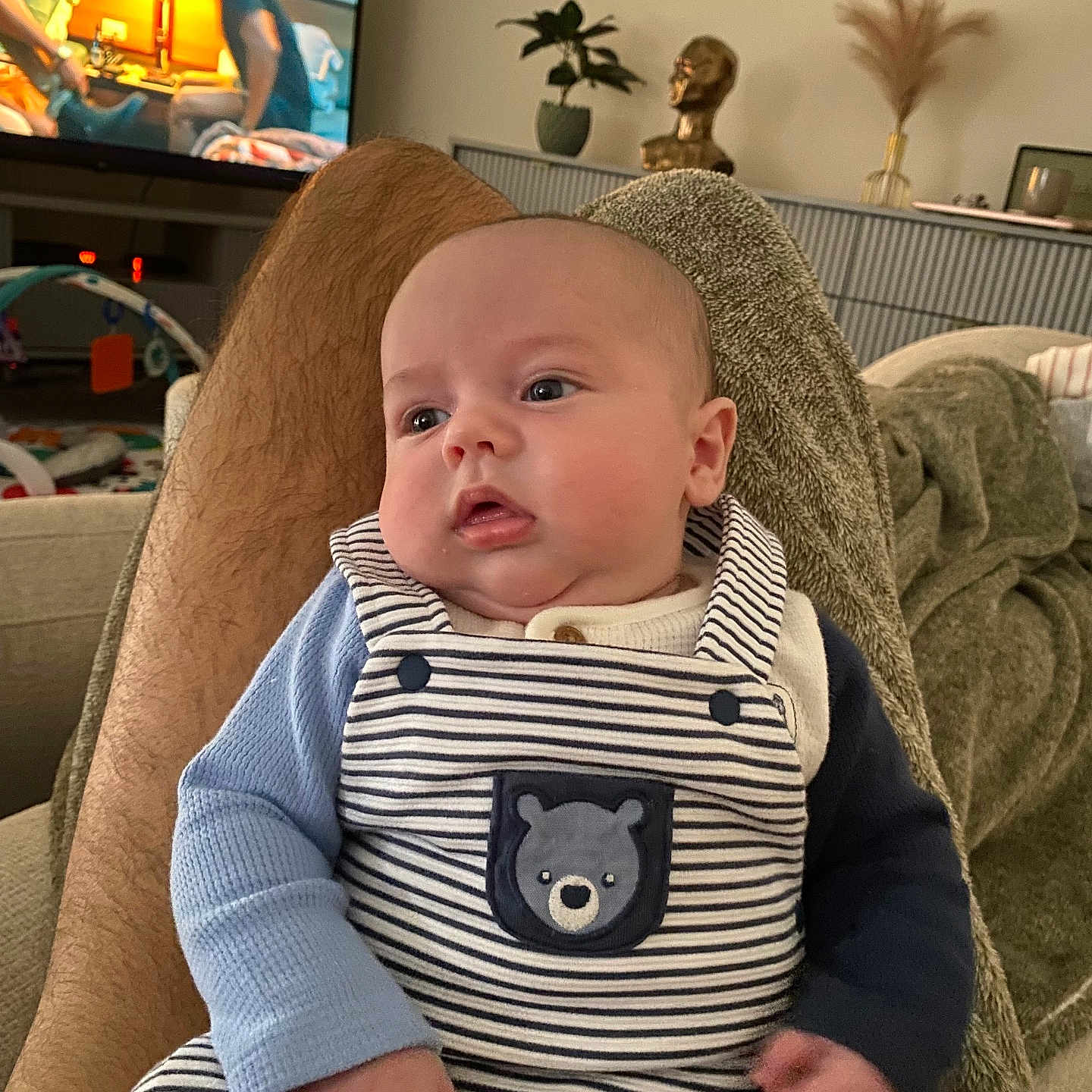 Télyo a rejoint le concours — aidez-le/la à gagner de superbes lots ! baby, bear_patch, blanket, casual, cozy, cushion, decor, face, hairy_legs, hand, indoors, infant, legs, living_room, person, plant, portrait, sofa, striped_overalls, television