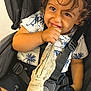 baby, car_seat, child, closeup, clothing, curly_hair, cute, fabric, face, hand, happy, indoor, person, playful, seatbelt, shirt, shorts, sitting, smiling, toddler