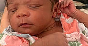 Keziah is registered to the contest to win money with this photo: baby, child, closeup, colorful, curly_hair, cute, floral_outfit, hand, holding, indoors, infant, newborn, patterned_clothing, peaceful, person, portrait, resting, skin, sleeping, soft_light