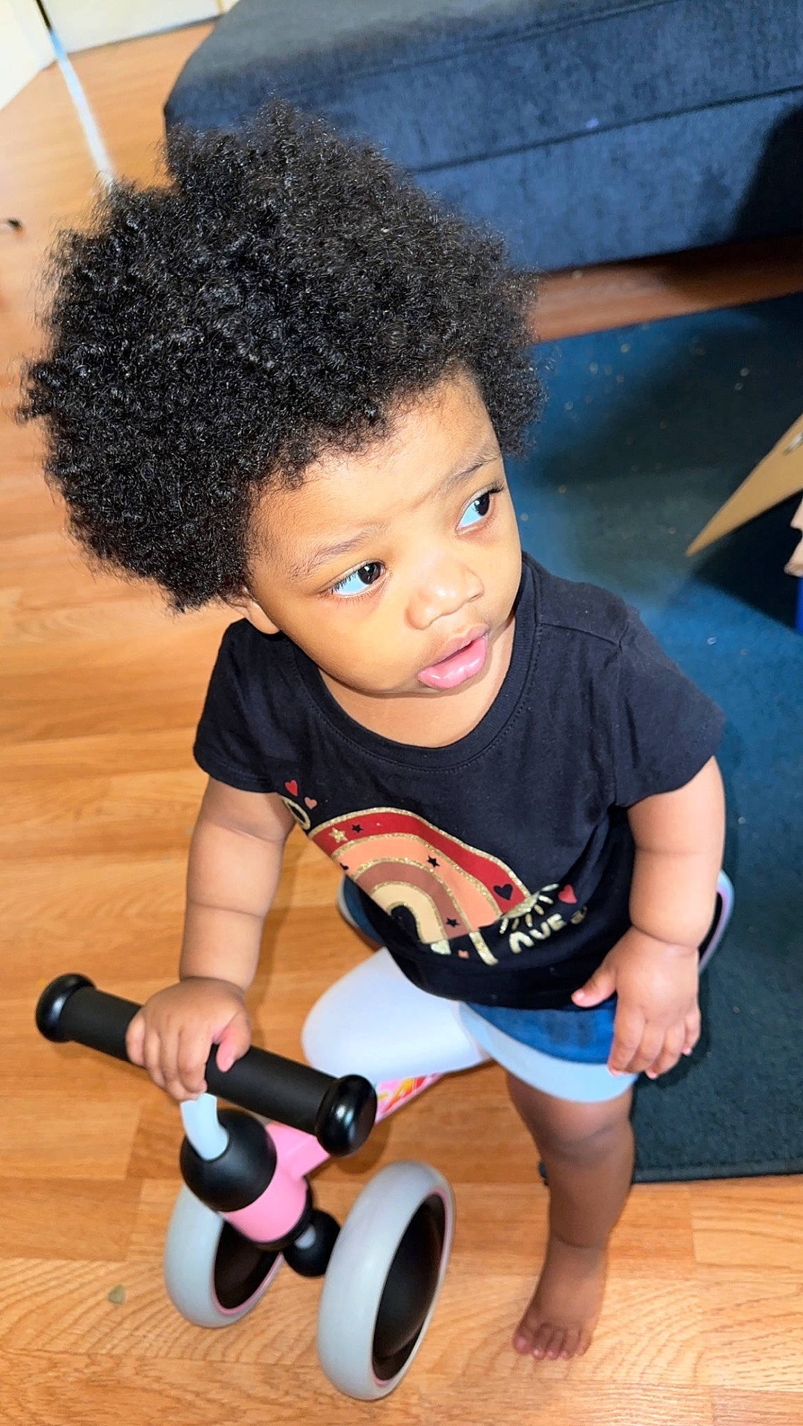 Aries is registered to the contest to win money with this photo: afro, arm, baby_toddler_clothing, black, chin, facial_expression, finger, floor, flooring, fun, human_body, person, skin, smile, thigh, tire, toddler, toy, wheel, wood