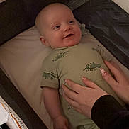 Nolan joined the competition — help win amazing prizes! baby, infant, smile, onesie, bassinet, crib, blanket, hand, nail_art, adult_hand, mesh_side, mattress, clothing, portrait, lying_down, indoor, soft_lighting, cute, face, pacifier