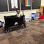 Alaya is registered to the contest to win money with this photo: toddler, child, wagon, classroom, carpet, posters, storage_bins, smile, happy, educational, indoor, toy, person, colorful, basketball_poster, numbers_chart, floor, handle, hair_buns, wall