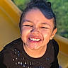 Dakota joined the competition — help win amazing prizes! child, smiling, laughing, portrait, close_up, face, eyes_closed, teeth, curly_hair, dark_hair, earrings, black_shirt, sparkly_clothing, yellow_chair, outdoor, greenery, sunlight, happy, joyful, photography