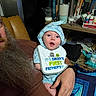 Joshua joined the competition — help win amazing prizes! baby, child, beard, bib, blue_clothing, man, adult, sitting, chair, bookshelf, books, bottle, indoor, facial_hair, hand, expression, happy, person, clothing, portrait