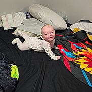 Joshua is registered to the contest to win money with this photo: baby, child, smiling, onesie, bed, blanket, pillow, indoor, happy, infant, person, cute, toddler, face, sleepwear, home, colorful, resting, lying, cozy