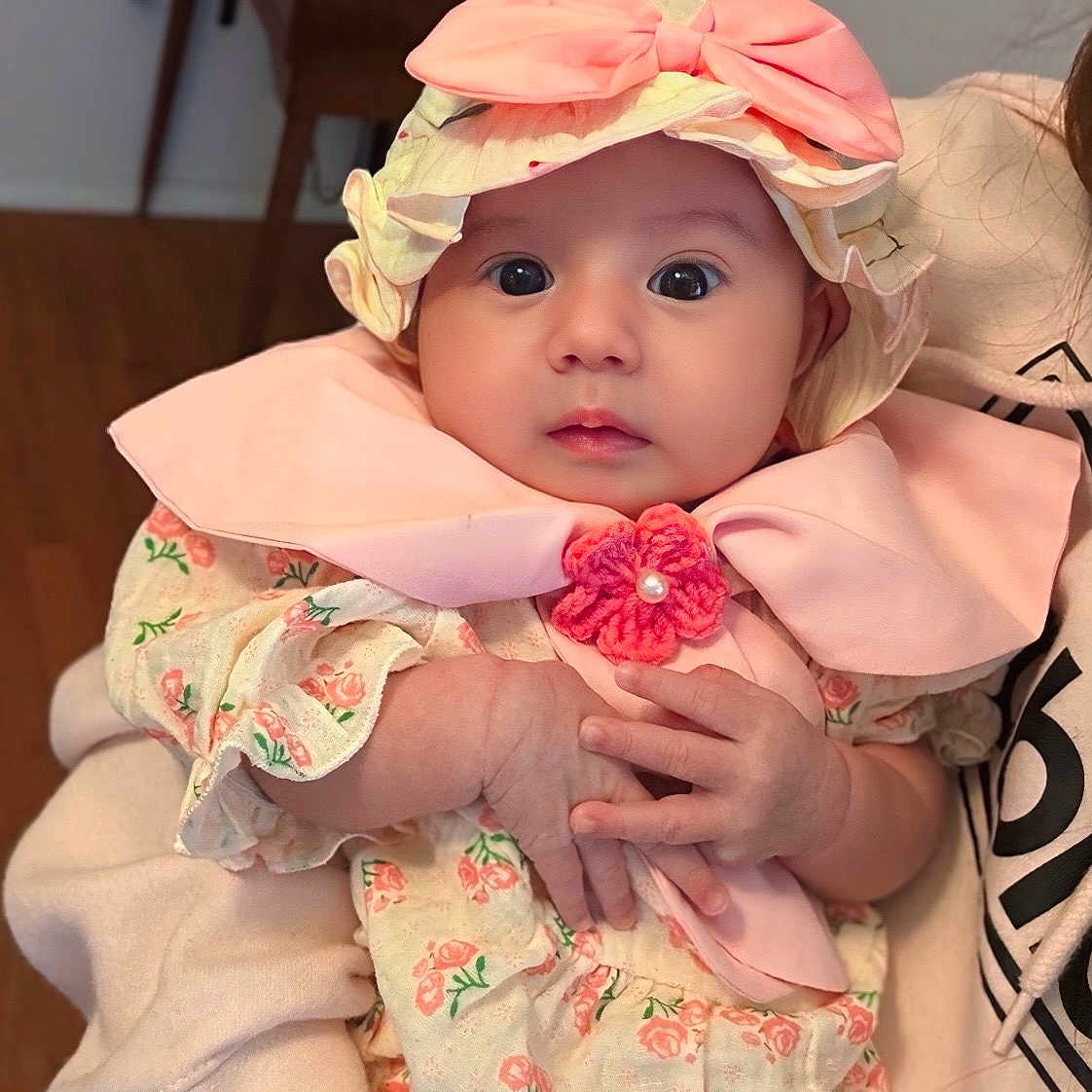 Lilian is registered to the contest to win money with this photo: apparel, baby, bow, child, clothing, cute, expression, eyes, face, floral, hands, hat, holding, indoor, infant, person, pink, portrait, sitting, soft_lighting