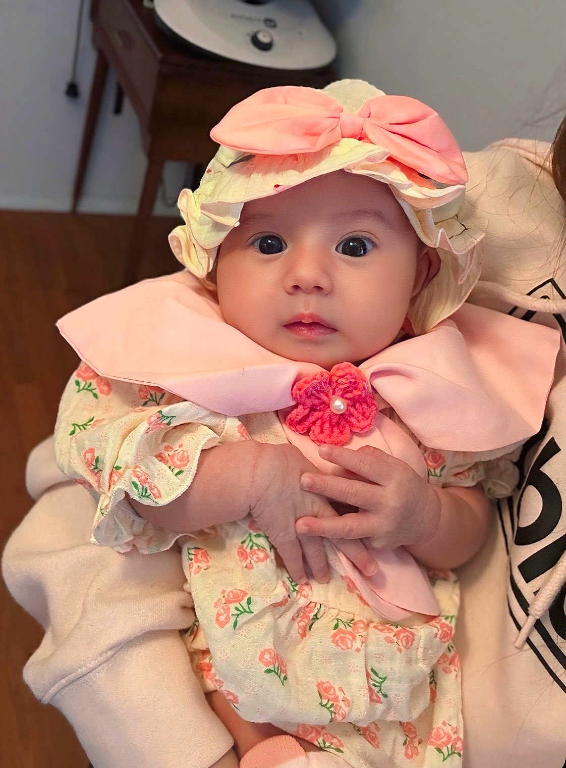 Lilian is registered to the contest to win money with this photo: baby, infant, child, hat, bow, pink, floral, clothing, hands, face, eyes, person, cute, indoor, soft_lighting, holding, portrait, expression, sitting, apparel