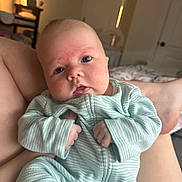 Emmaline is registered to the contest to win money with this photo: baby, infant, onesie, striped_clothing, hands, face, eyes, bedroom, bed, blanket, parent_leg, newborn, portrait, close_up, soft_light, cheeks, pajamas, crib, calm, indoors