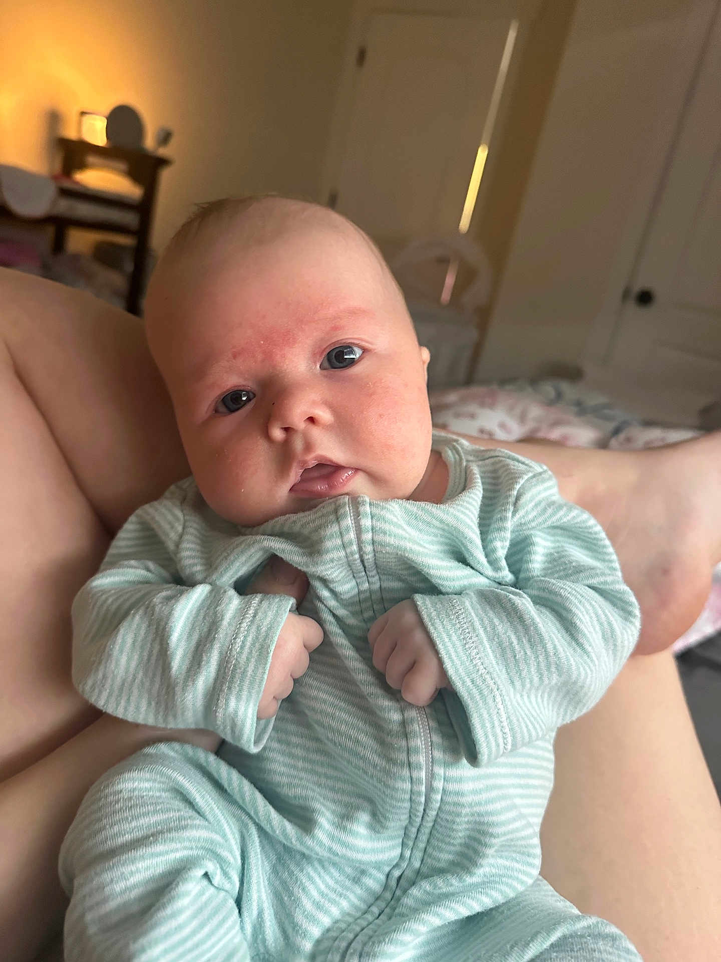 Emmaline is registered to the contest to win money with this photo: baby, infant, onesie, striped_clothing, hands, face, eyes, bedroom, bed, blanket, parent_leg, newborn, portrait, close_up, soft_light, cheeks, pajamas, crib, calm, indoors