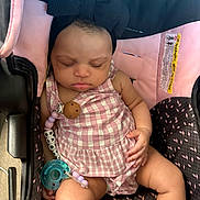 Sagelyn is registered to the contest to win money with this photo: baby, sleeping, car_seat, pacifier, headband, bow, pink, checkered, clothing, child, infant, cute, peaceful, resting, seat, strap, accessory, indoors, person, portrait