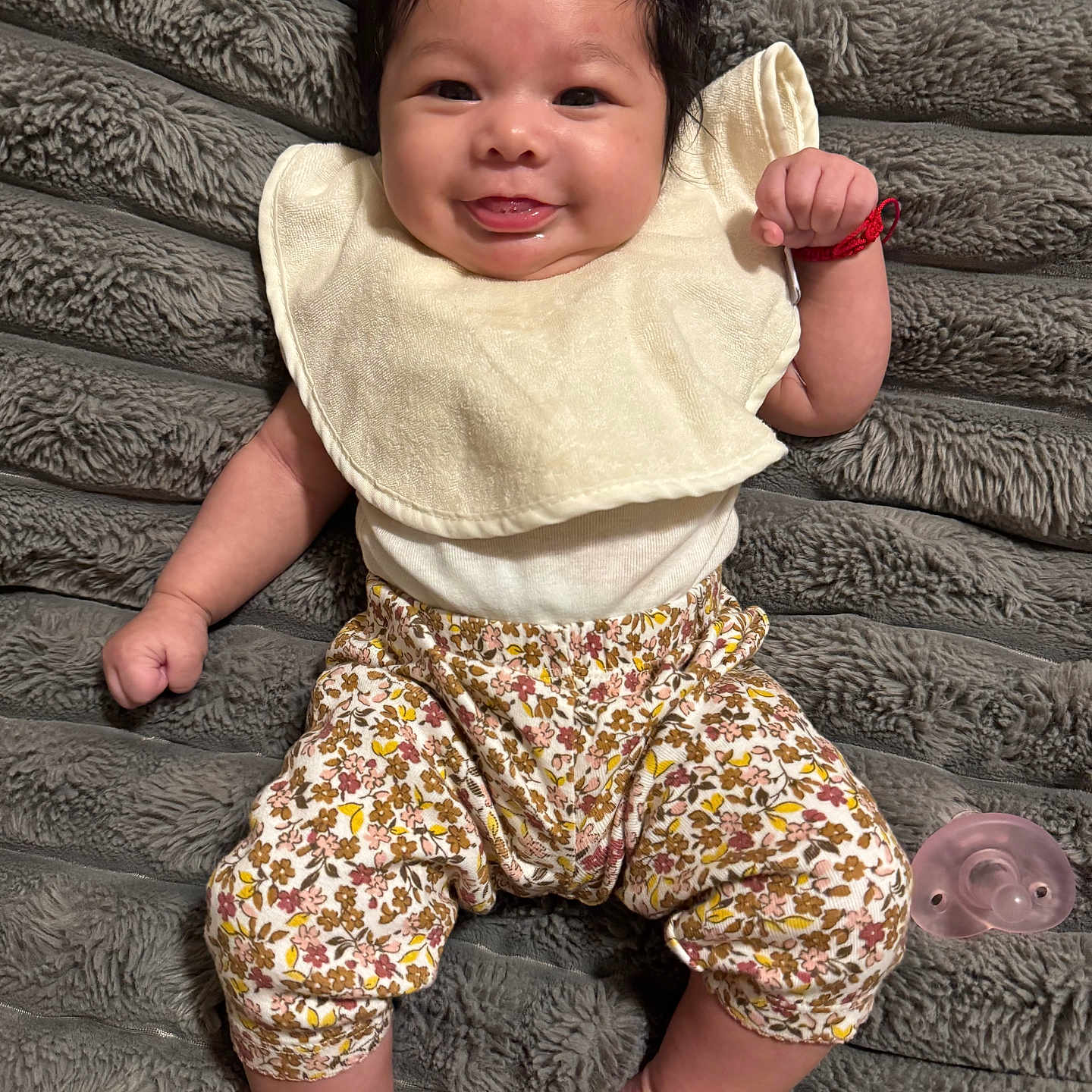 Xamora joined the competition — help win amazing prizes! baby, bib, blanket, clothing, comfort, cute, dark_hair, face, fist, floral_pants, foot, hand, happy, indoors, infant, lying_down, pacifier, skin, smiling, texture