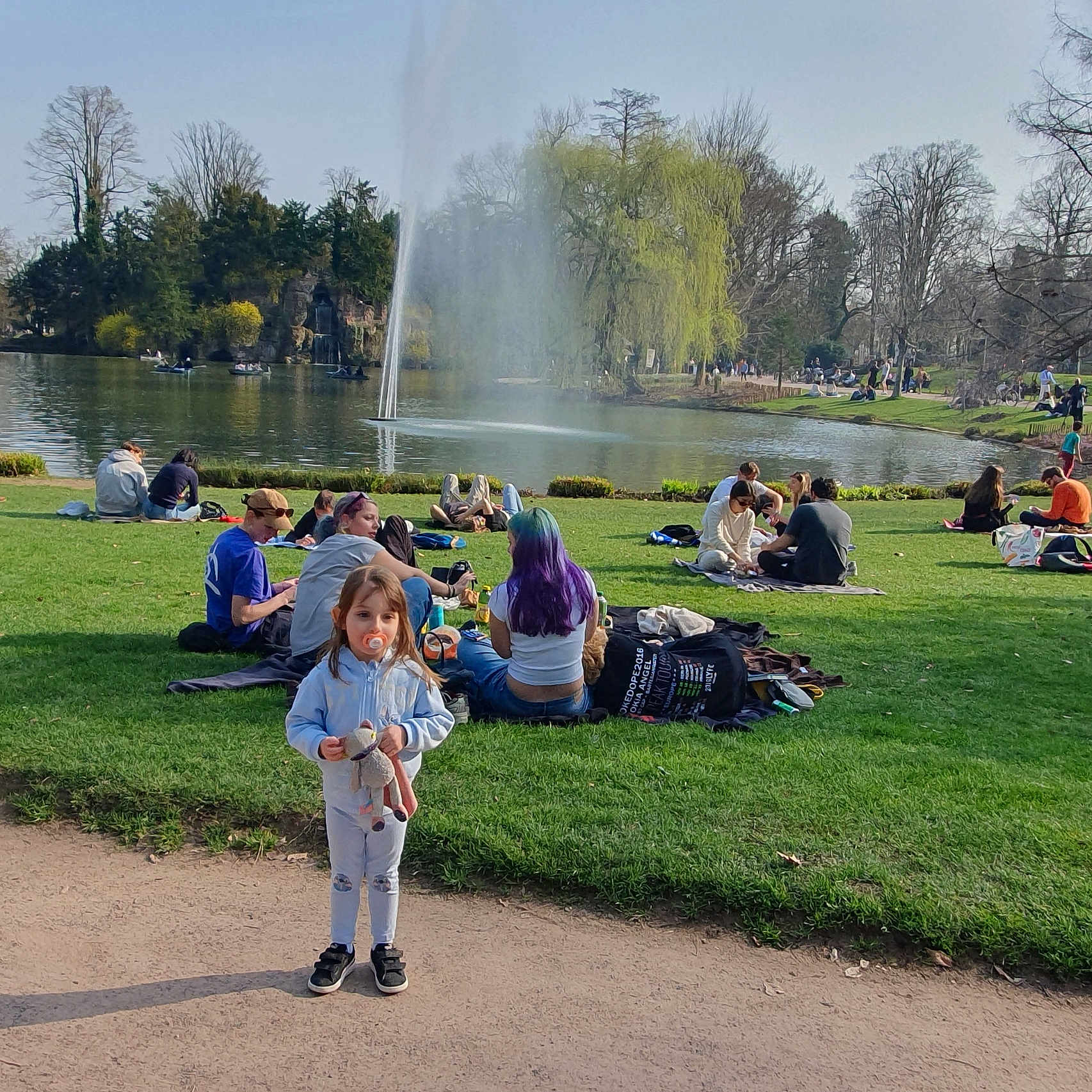 Mayla a rejoint le concours — aidez-le/la à gagner de superbes lots ! casual_clothing, child, daytime, family, fountain, grass, green_space, lake, outdoors, pacifier, park, people, picnic, relaxing, sitting, spring, stuffed_animal, toddler, trees, walking_path