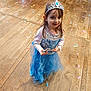 child, girl, princess, tiara, blue_dress, costume, confetti, wooden_floor, smile, wand, party, celebration, portrait, face, happy, long_hair, indoor, flooring, cute, event