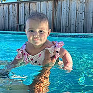 Anastasia is registered to the contest to win money with this photo: baby, child, swimming_pool, water, summer, outdoor, sunlight, reflection, polka_dot, swimsuit, cute, smiling, person, hand, skin, trees, fence, blue, daytime, recreation
