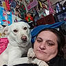 dog, person, indoor, selfie, white_dog, medals, drawings, wall_art, portrait, paw, furniture, decorations, cabinet, colorful, face, casual, expression, human, pet, closeup