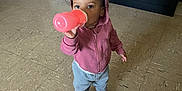 Nayla joined the competition — help win amazing prizes! casual_clothing, child, colorful_shoes, cute, daylight, drinking, floor, gray_pants, home, hoodie, indoor, person, pink_cup, pink_hoodie, shoes, socks, standing, tile_floor, toddler, young_child