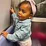 baby, child, clothing, curly_hair, cute, denim_jacket, face, headband, indoor, jacket, metal, person, pink, playful, portrait, public_transport, seat, smile, toddler, wall