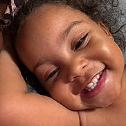 Nayla joined the competition — help win amazing prizes! child, smiling, close_up, curly_hair, happy, face, skin, arm, teeth, portrait, person, cute, joyful, expression, indoors, natural_light, relaxed, young, toddler, cheerful