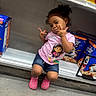 Nayla is registered to the contest to win money with this photo: child, girl, posing, pink_shirt, denim_shorts, pink_shoes, cereal_boxes, grocery_store, sitting, playful, peace_signs, curly_hair, smiling, shelf, food, packaging, store_aisle, casual_clothing, floor, young