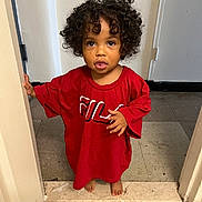 Nayla is registered to the contest to win money with this photo: barefoot, casual, child, clothing, curious_expression, curly_hair, cute, doorway, floor_tiles, hands, home, indoor, looking_up, oversized_clothing, person, portrait, red_tshirt, standing, toddler, young_child