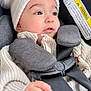 baby, infant, car_seat, hat, knit_hat, pom_pom, sweater, harness, buckle, hand, face, eyes, eyelashes, closeup, looking_away, adorable, winter_clothing, padding, warning_label, cozy