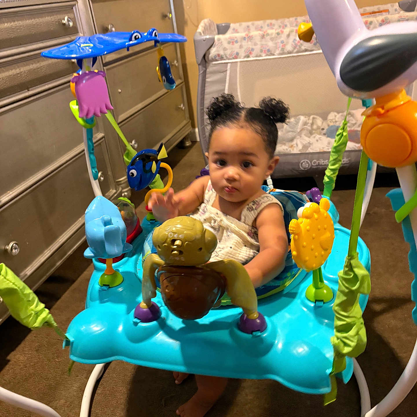 Shaharie is registered to the contest to win money with this photo: activity_jumper, baby, carpet, child, clothing, colorful, cute, dresser, floor, fun, hair_buns, indoor, infant, person, plastic_toy, playpen, room, toddler, toy, young_child