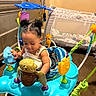 activity_center, baby, baby_equipment, cabinets, carpet, child, clothing, colorful, curly_hair, double_buns, floor, home, indoor, infant, plastic_toys, playpen, playtime, seat, toddler, toys