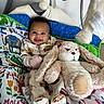 baby, smiling, plush_toy, bunny, pajamas, blanket, colorful, indoor, child, cute, happy, lying_down, soft_toy, animal_print, face, infant, cozy, playful, comfort, funny_expression