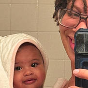 Evelina is registered to the contest to win money with this photo: baby, towel, smiling, glasses, adult, child, mirror, bathroom, selfie, person, face, skin, eyes, hand, portrait, curly_hair, closeup, indoor, happy, holding