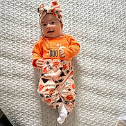 Leah joined the competition — help win amazing prizes! baby, infant, smiling, orange_clothing, headband, bow, halloween_theme, pumpkin, spider_web, white_socks, lying_down, mattress, patterned_mattress, cute, happy, indoor, child, person, festive, portrait