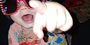 Kinlinn is registered to the contest to win money with this photo: toddler, child, sunglasses, pointing, smiling, pink, colorful, clothing, indoors, padded_rail, joyful, playful, face, hand, person, expression, casual, fun, toy, background