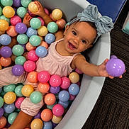Amari joined the competition — help win amazing prizes! toddler, child, ball_pit, colorful_balls, smiling, happy, headband, bow, play, indoor, pink_clothing, pastel_colors, skin, person, fun, cute, young_child, reaching_out, carpet, joyful