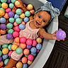 toddler, child, ball_pit, colorful_balls, smiling, happy, headband, bow, play, indoor, pink_clothing, pastel_colors, skin, person, fun, cute, young_child, reaching_out, carpet, joyful